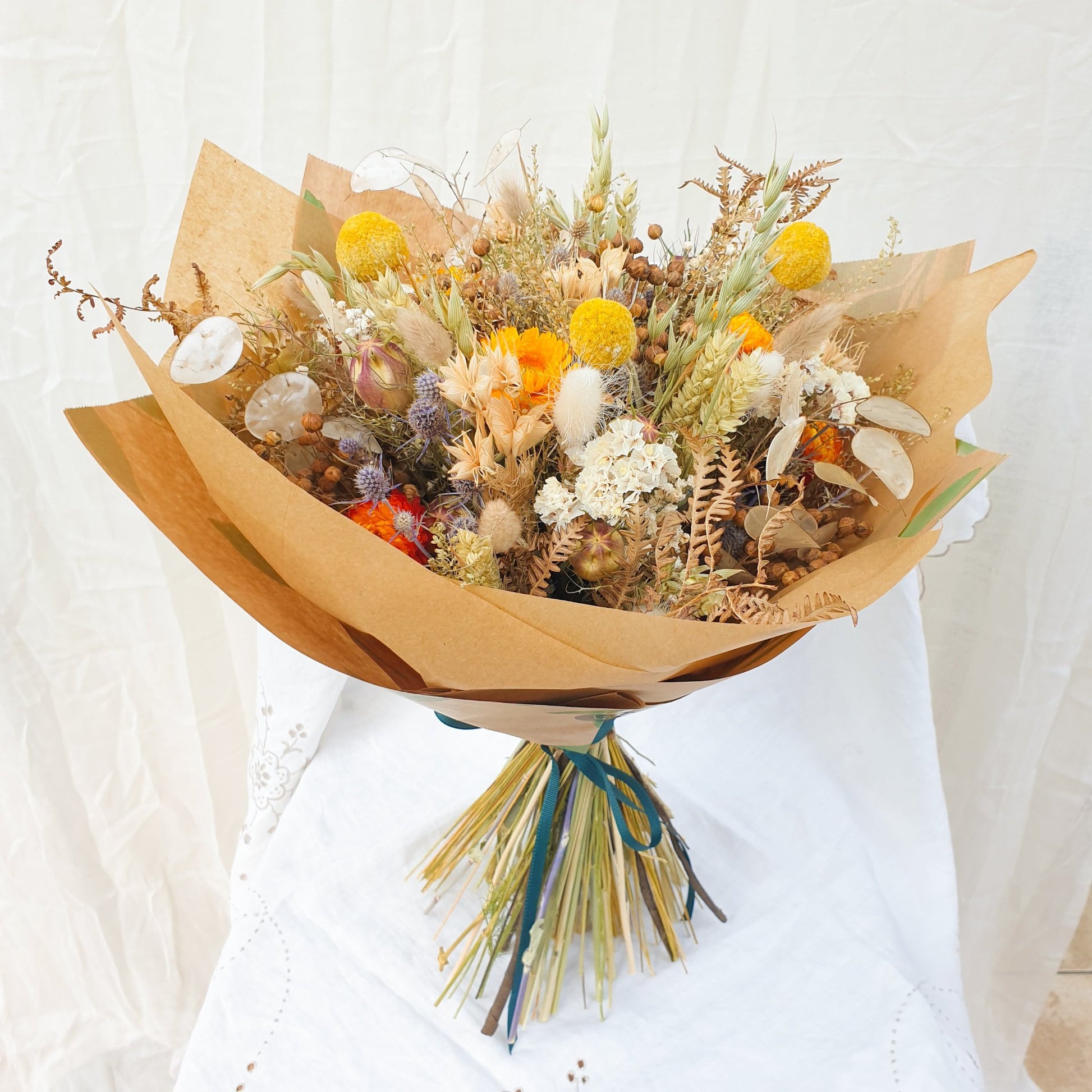 The large bouquet is shown wrapped stylishly in recycleable brown paper wrap. It is tied with a pretty slim green ribbon wrapped around the stems a few times.