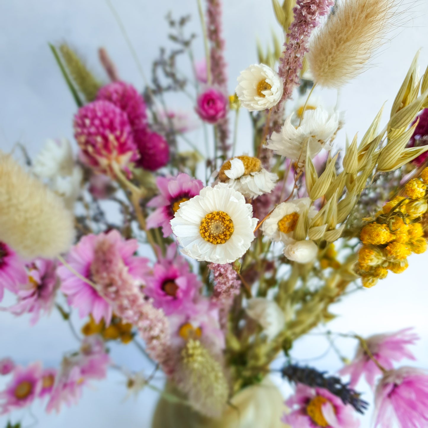 Dried Flower Mixed Box- Wildflower Fields by Lytton Rose Botanical. A close-up image highlighting the intricate details of a dried flower arrangement. Delicate white daisies with yellow centers take center stage, surrounded by soft, fluffy dried grasses and other pink daisies, yellow lona and lavender coloured flowers.